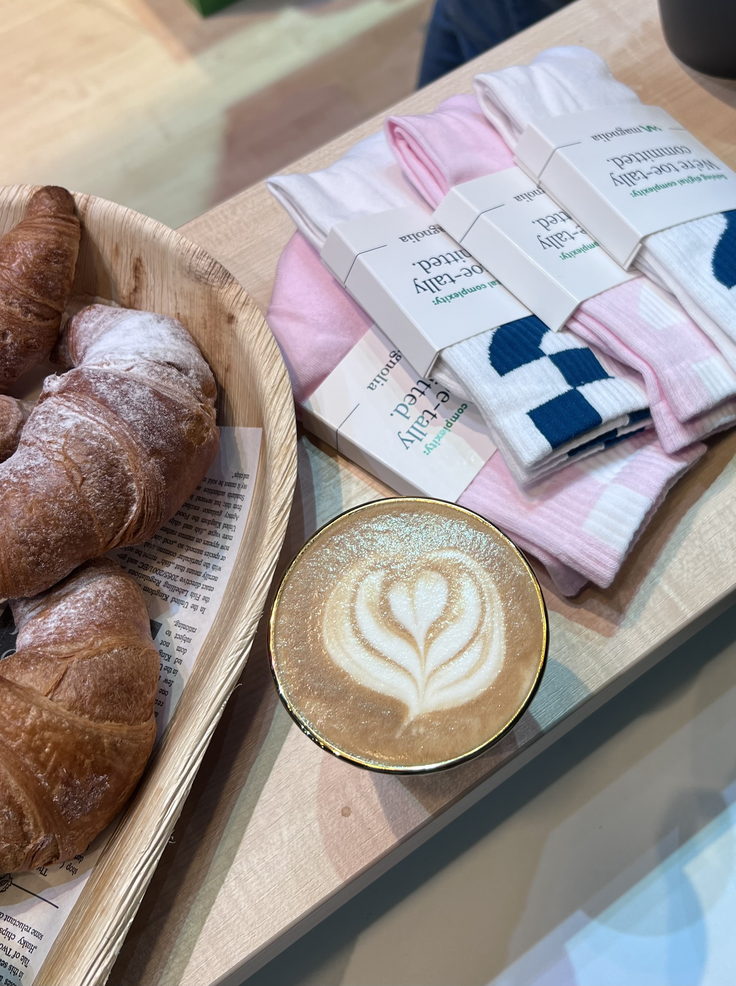 Espresso art, croissant, and Magnolia branded socks on a wooden table